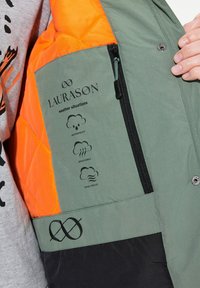 Grön och orange jacka med en dragkedjeficka. Har ikoner för vattentäta, andningsbara och vindskyddande egenskaper; logotypen visas.