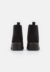 Stivali neri alla caviglia in un mix di camoscio e materiale elastico a coste, con un tacco spesso e un accent metallic alla base.