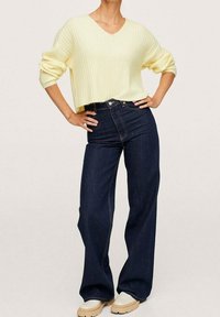 Pullover a coste giallo chiaro con scollo a V, abbinato a jeans a gamba larga blu scuro e scarpe platform beige. Look casual e comodo.