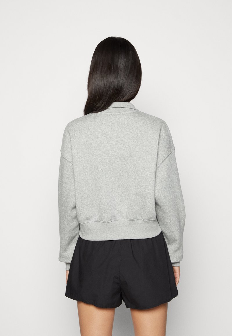 Sudadera gris de mangas largas y cuello redondo, con un dobladillo acanalado. Combinada con pantalones cortos negros. Diseño simple y casual.