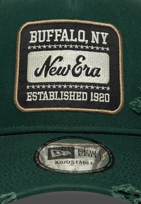 Casquette verte avec une patch brodé noir et blanc portant l'inscription "Buffalo, NY New Era Established 1920", dotée d'une taille ajustable et d'un tissu texturé.