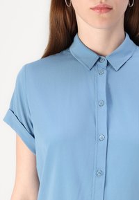 Light blue short-sleeve shirt with a button-up front, collar, and soft texture. Features rolled cuffs and matching buttons.