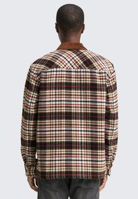 Beige, braun und rot karierte Flanellhemd mit einem Rippkragen. Lange Ärmel mit Knopfmanschetten, die ein großes Karomuster zeigen.