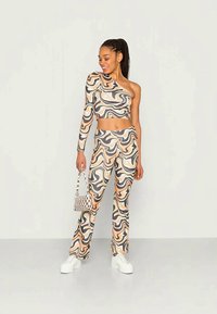 Conjunto de duas peças com um top cropped de um ombro só e calças boca de sino. O tecido apresenta um padrão ondulado em tons terrosos de bege, castanho e cinza.