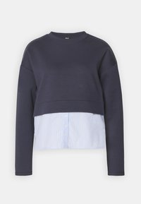 Sweat-shirt court bleu marine à manches longues, avec un bas superposé à rayures bleu clair et blanc, et une fermeture à boutons.