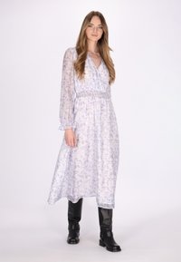 Hellblaue Blumenkleid mit Midi-Länge, langen Ärmeln und elastischem Bund. Kombiniert mit schwarzen kniehohen Stiefeln, vor einem neutralen Hintergrund.