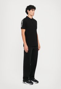 Black polo shirt with short sleeves, featuring a striped design on the shoulders, paired with black pants and black athletic shoes.