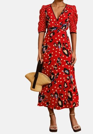 Donna che indossa un vestito midi rosso con maniche a sbuffo, pois, stampe astratte, tiene una borsa intrecciata con manici neri e indossa sandali beige con tacco.
