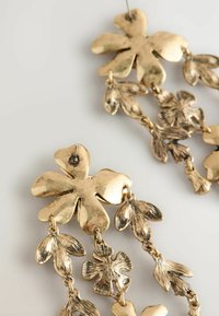 Goldfarbene Ohrringe mit floralem Design, die oben eine große Blüte und darunter kaskadierende kleinere Blüten aufweisen. Glatte und strukturierte Oberflächen.