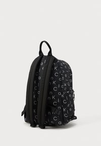 Μαύρος σάκος πλάτης με λευκό σχέδιο λογότυπου, επενδεδυμένη πλάτη και ιμάντες ώμου. Περιλαμβάνει μια πλευρική τσέπη και μια λαβή στη κορυφή.