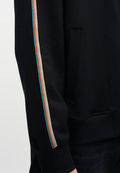 Μαύρο φούτερ με τσέπη καγκουρό και πολύχρωμες κάθετες ρίγες σε πορτοκαλί, μπλε και μπεζ κατά μήκος των μανικιών.