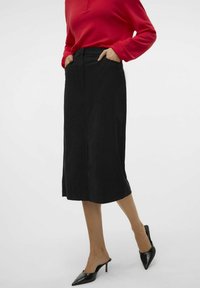Černá tužková sukně s rovný střih, detail předního rozparku a bočními kapsami. V kombinaci s černými jehlovými podpatky a červeným svetrem s dlouhým rukávem.