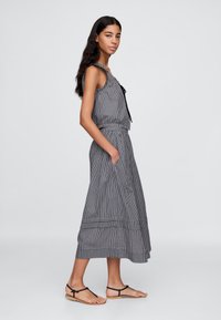 Svartvit rutig ärmlös topp med knytning och matchande lång kjol med sidofickor, komplterat med platta sandaler med remmar.