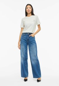 Jasnoszara koszulka z grafiką kwiatową, zestawiona z wysokim stanem, szerokimi nogawkami w niebieskich jeansach oraz czarnymi szpilkami z ostrym noskiem. Prosty, codzienny strój.