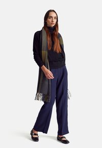 Czarny sweter z golfem, spodnie w kolorze granatowym o wysokim stanie oraz szary szalik w kratę z frędzlami; czarne baleriny z srebrnymi klamrami.