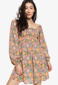 Vestido floral con mangas largas abullonadas; presenta flores multicolores en amarillo, rosa y verde sobre un fondo claro; cintura elástica.