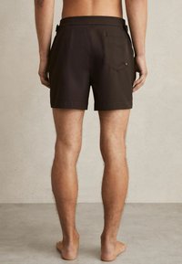 Șorturi de baie maro închis, cu o textură netedă, talie elastică și un singur buzunar în spate. Prezintă un design minimalist și un material moale.