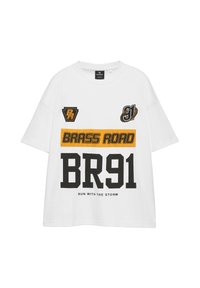 T-shirt blanc à manches courtes avec texte noir et jaune « BRASS ROAD », « BR91 » et « RUN WITH THE STORM » et deux petits patchs graphiques sur la poitrine.