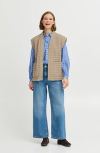 Gilet matelassé beige sans manches, associé à une chemise bleue à rayures et un jean en denim à jambes larges. Il dispose de poches et d'un ajustement décontracté.