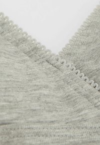 Šedá pletená látka s výstřihem do V a vroubkovaným lemem. Disponuje jemnou strukturou a diagonálním vzorem.