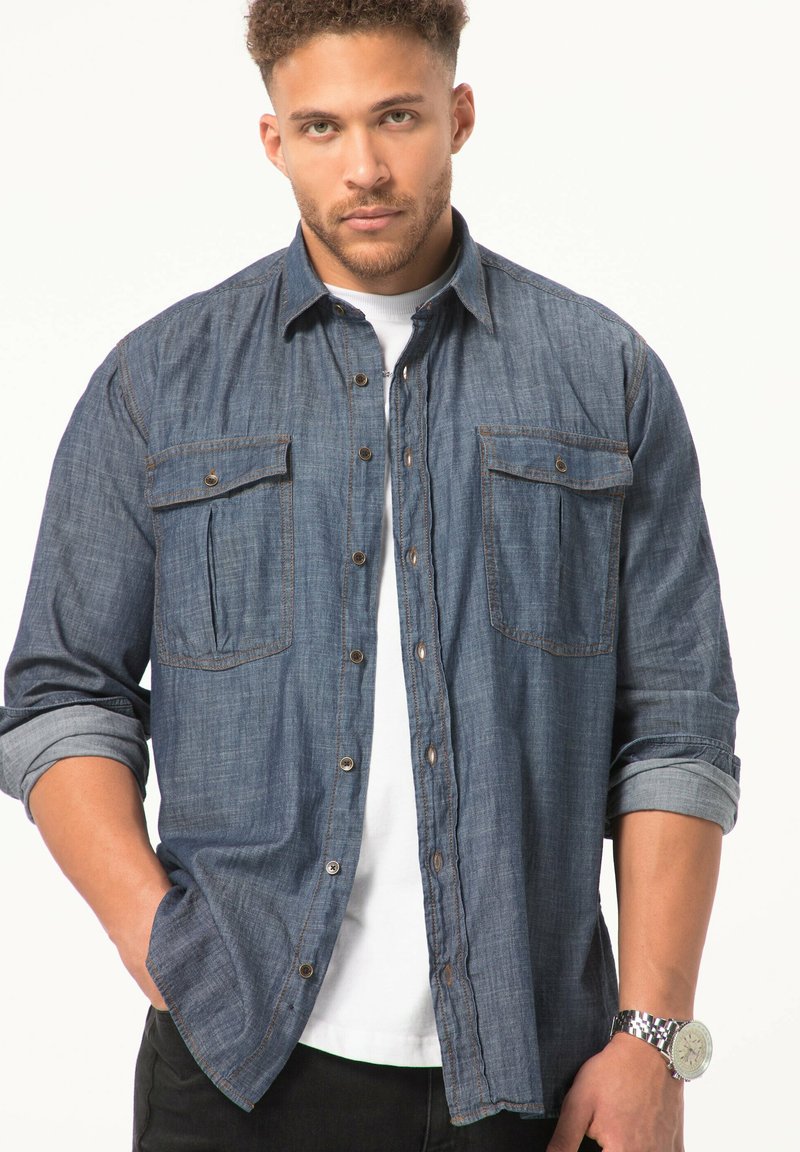 Dunkelblaue Jeanshemd mit Knopfleiste, zwei Brusttaschen, aufgerollten Ärmeln, kontrastierenden Nähten und abgenutztem Look, kombiniert mit einem weißen T-Shirt.