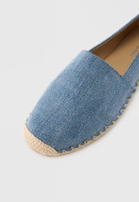 Espadrila od trapera s okruglim vrhom i đonom od tkanog juta. Svijetloplava tkanina, jednostavno šivanje po gornjem dijelu i prirodna tekstura.