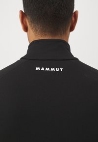 Must mustrõngas, millel on kõrge krae ja valge "MAMMUT" logo seljal. Sile tekstuur, kehakujuline disain ja minimaalsed õmblusdetailid.