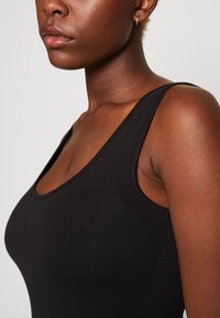 Black sleeveless top made of smooth fabric. Features a scoop neckline and a fitted design with clean edges and a seamless look.