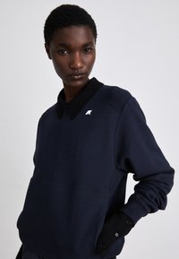 Felpa navy con colletto nero, polsini a coste e un piccolo logo sul petto. Presenta una superficie liscia e una vestibilità comoda.