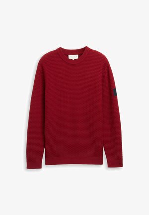 Pulover texturat roșu cu guler rotund, mâneci lungi, manșete ribbate și un accent albastru închis pe mâna stângă.