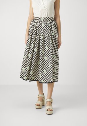 Femme portant une jupe midi à carreaux noir et blanc avec une taille froncée, associée à un haut sans manches blanc et des talons compensés beige.