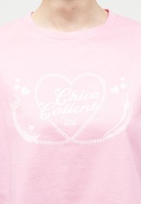 Ροζ πουκάμισο με λευκό τυπωμένο σχέδιο δύο πλεγμένων καρδιών, μικρές καρδιές, τσίλι και κείμενο "Chica Caliente ΚΑΛΕΣΤΕ ΤΩΡΑ!"