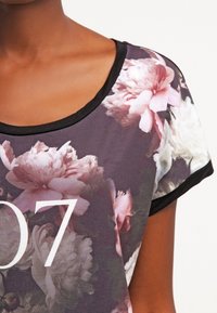 Primer plano de una camisa con estampado floral y ribete negro en el collar y las mangas, que presenta grandes flores rosas y blancas y el número "07".