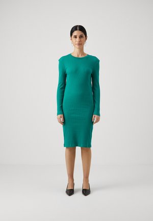 Teal ribbestrikket kjole med lange ermer og rund hals, tettsittende til kroppen, som når midt på leggen. Satt sammen med svarte spisse hæler.