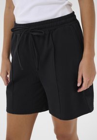 Shorts en coton noirs avec une taille élastique et un cordon de serrage, comprenant des poches latérales et un ourlet droit. Texture douce et coupe décontractée.