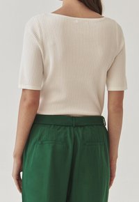 Ribbade vita toppar med korta ärmar och vid halsringning, i kombination med gröna högmidjade byxor med bakfickor och en avslappnad passform.