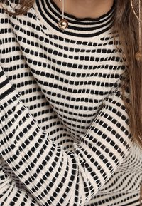 Gebreide trui met een geribde kraag, horizontale zwart-witte strepen en een textuurpatroon. Lange mouwen tonen een gelijkmatige striping.
