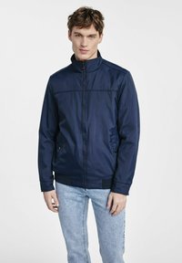 Granatowa kurtka zapinana na zamek z kołnierzem typu stojącego, bocznymi kieszeniami i ściągaczami. Gładka tekstura, lekki materiał i proste detale przeszyć.