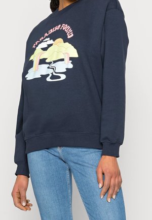 Marineblauwe sweater met de tekst "Paradise Found", met een afbeelding van bergen, watervallen, wolken en een opkomende zon in pastelkleuren.
