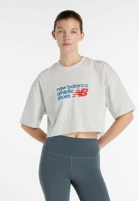 Grijze cropped t-shirt met een blauw en rood "new balance athletic shoes" graphic. Gecombineerd met hoge, donkergroene leggings. Glad textuur.