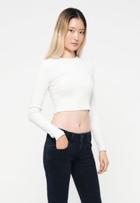 Top blanco corto de manga larga en textura acanalada combinado con jeans ajustados de color azul oscuro. Diseño ceñido, mínimos detalles y colores sólidos.