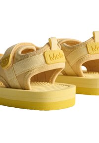 Gule sandaler med et teksturert stoffoverdel, justerbare stropper og en polstret såle med rillede mønstre. Merkbar merkevaredetalj synlig.