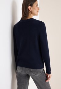 Mörkblå tröja med mjuk textur, rund halsringning och ribbade manschetter. Matchas med grå denimjeans med bakfickor.