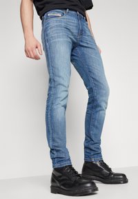 Jean skinny en denim bleu clair avec une finition délavée, design à cinq poches et coutures contrastées, associés à des bottes noires à lacets.