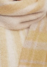 Écharpe douce et épaisse avec un motif à carreaux beige et jaune clair enroulée autour du cou ou de la zone du col.