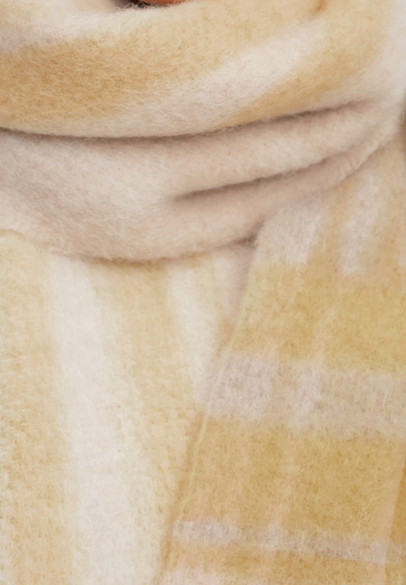 Écharpe douce et épaisse avec un motif à carreaux beige et jaune clair enroulée autour du cou ou de la zone du col.