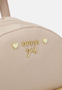 Bolso de piel sintética rosa con costuras en relieve, logo dorado "GUESS" y acentos en forma de corazón. Textura suave con un acabado sutilmente brillante.