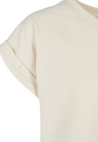 T-shirt beige en coton à manches courtes avec revers roulés et col rond, montrant un détail du haut du torse.