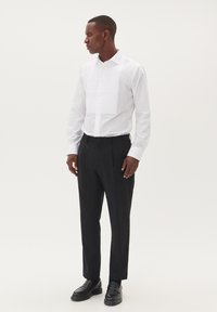 Balta krekla ar teksturētu krokām priekšā, apvienota ar melnām biksēm un melniem mokasīniem. Gluda auduma un klasiskā apkakles dizains.