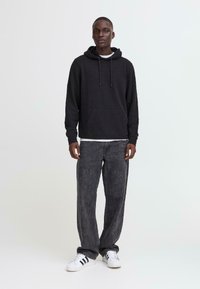 Svart hettegenser med frontlomme, kombinert med mørkegrå jeans og hvite sneakers med svarte striper. Enkel, avslappet passform.